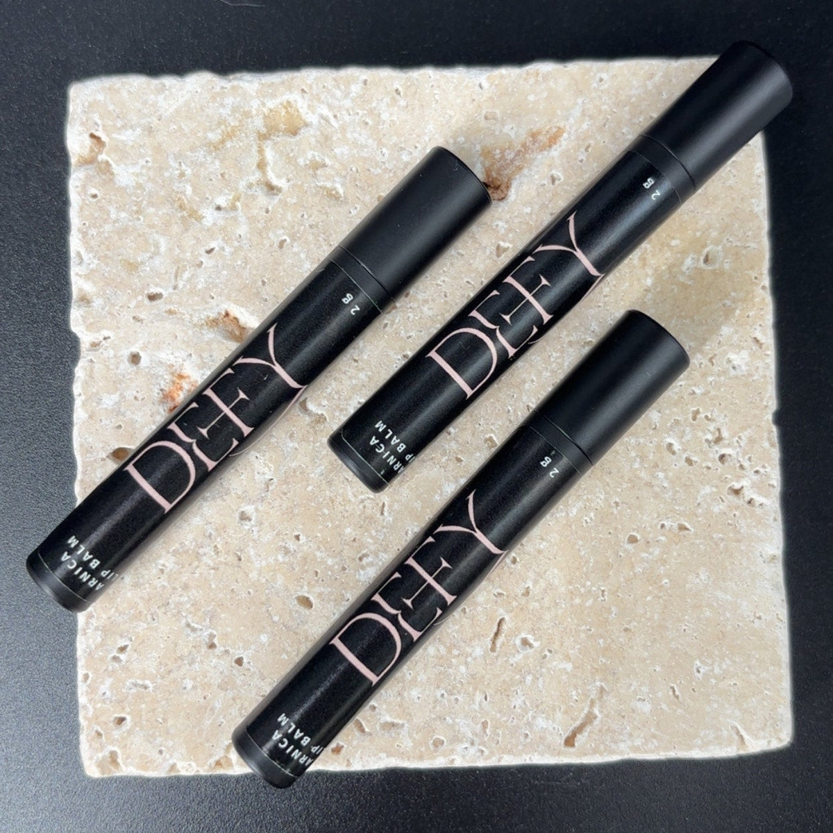 Four black  lip products on a beige stone surface with a black background